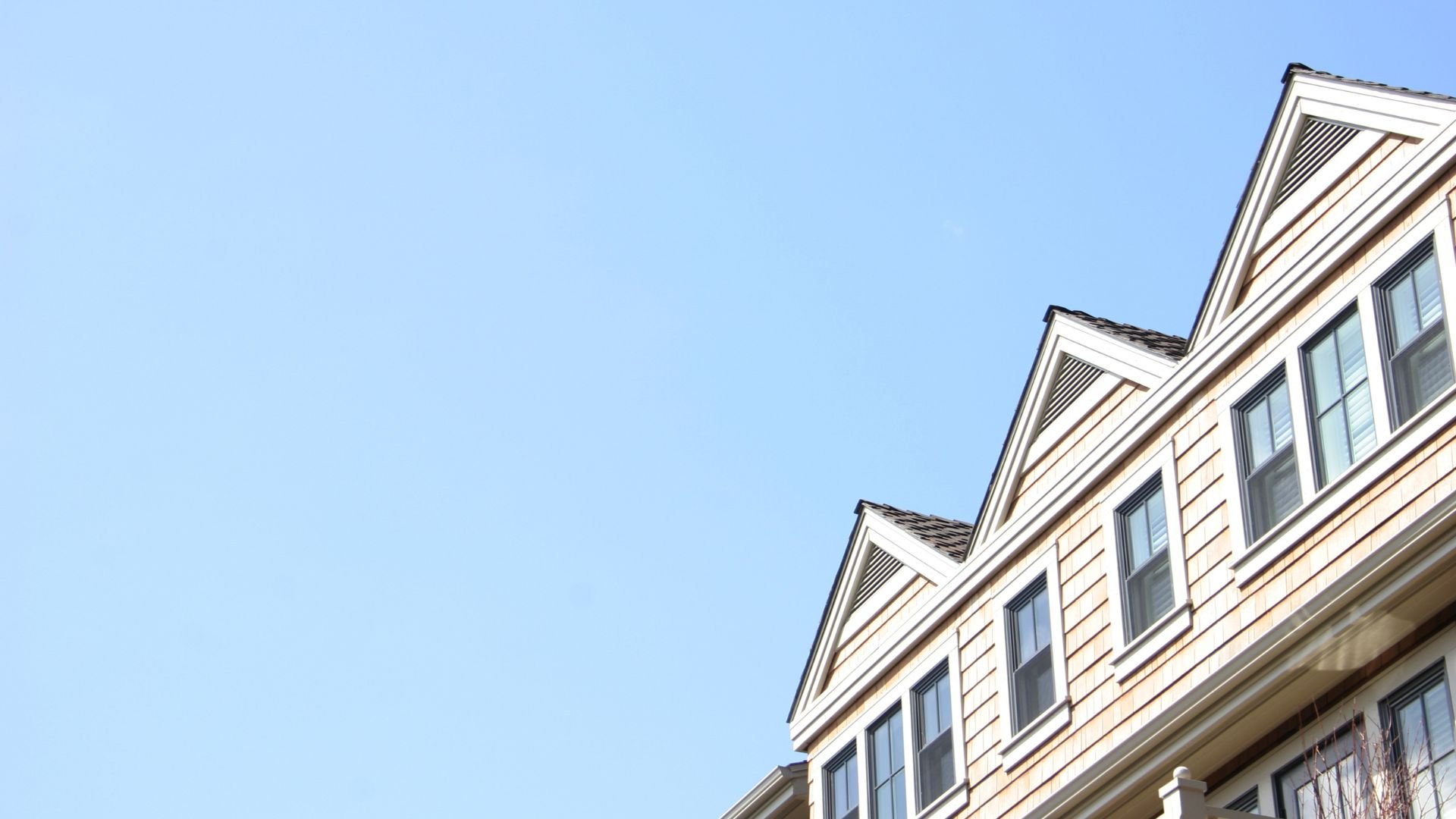 Beige wooden house with multiple gabled roofs against clear blue sky