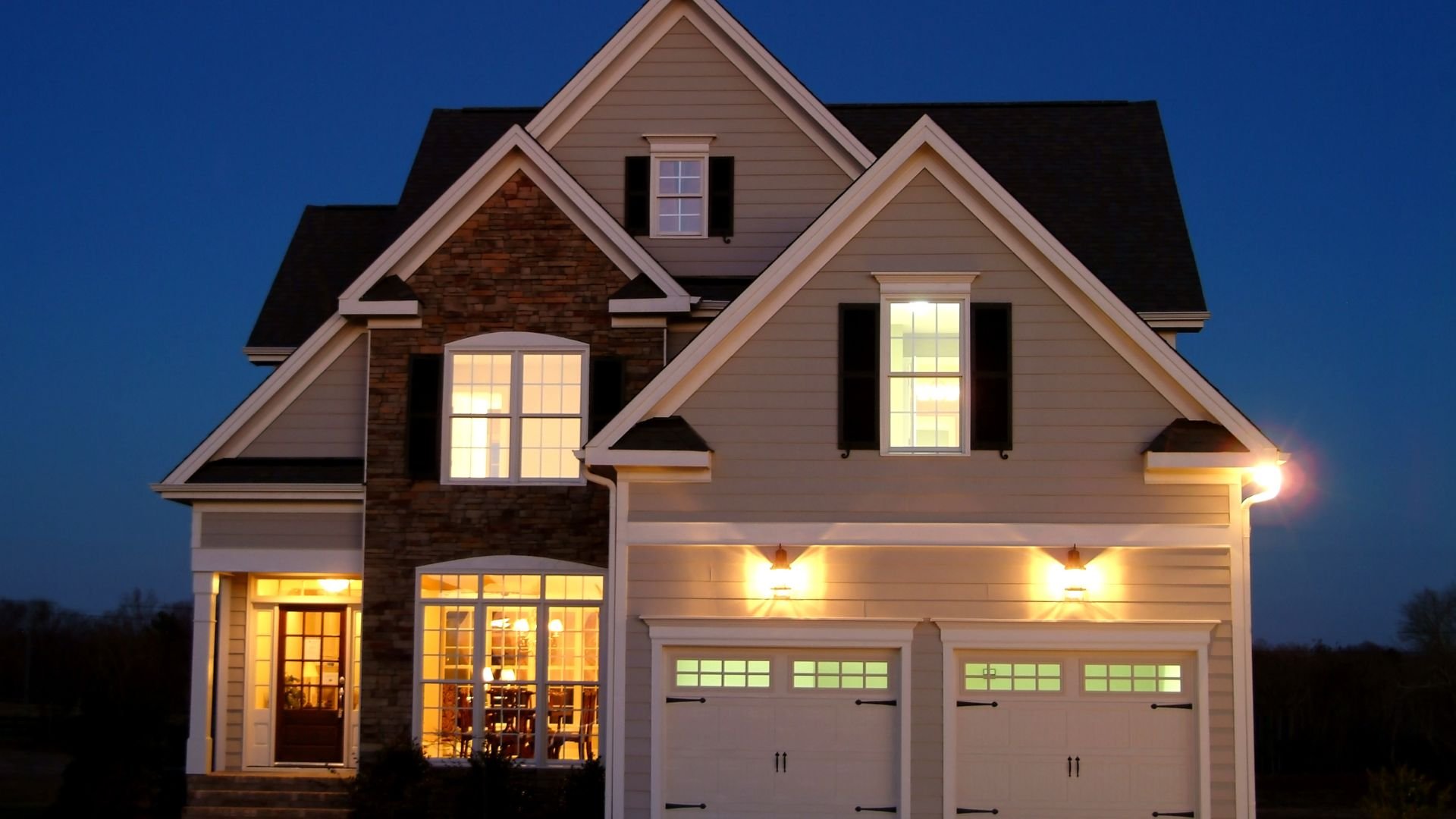 Warm two-story house with glowing windows at twilight, stone and siding exterior