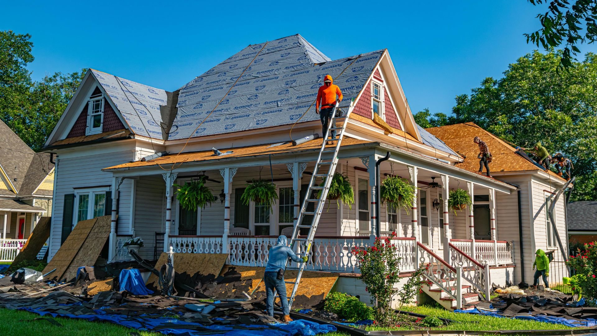 Workers replace roof on historic white house with ornate porch