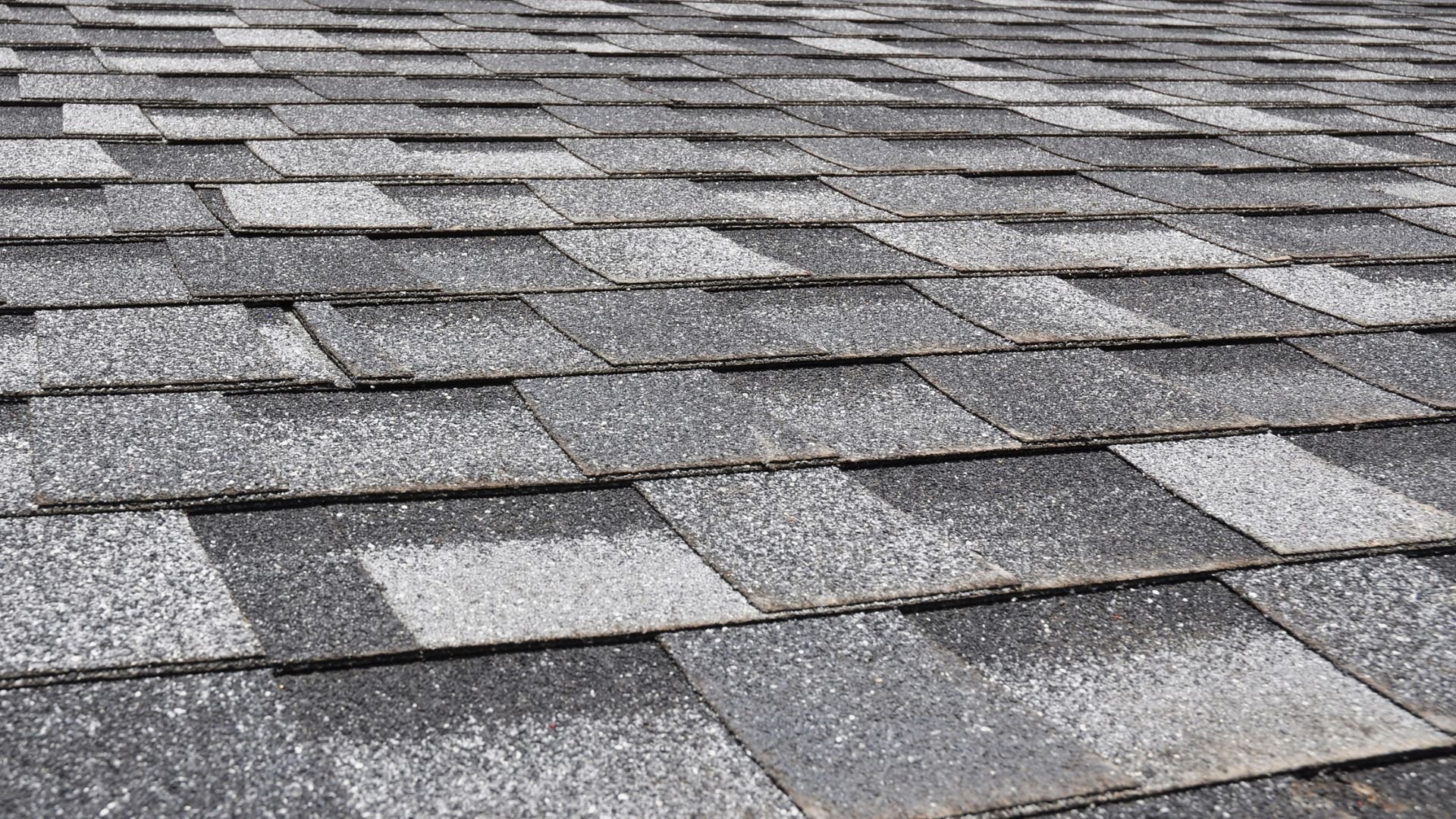 Gray asphalt roof shingles overlapping in a textured pattern