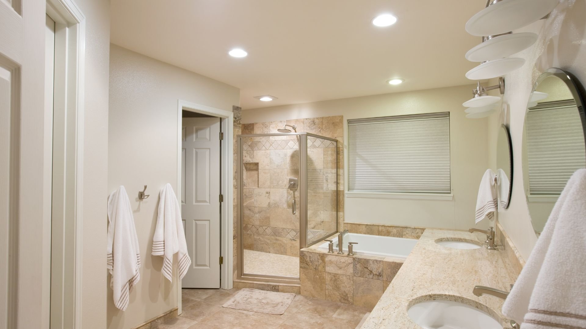 Spacious bathroom with glass shower, marble tiles, and white towels