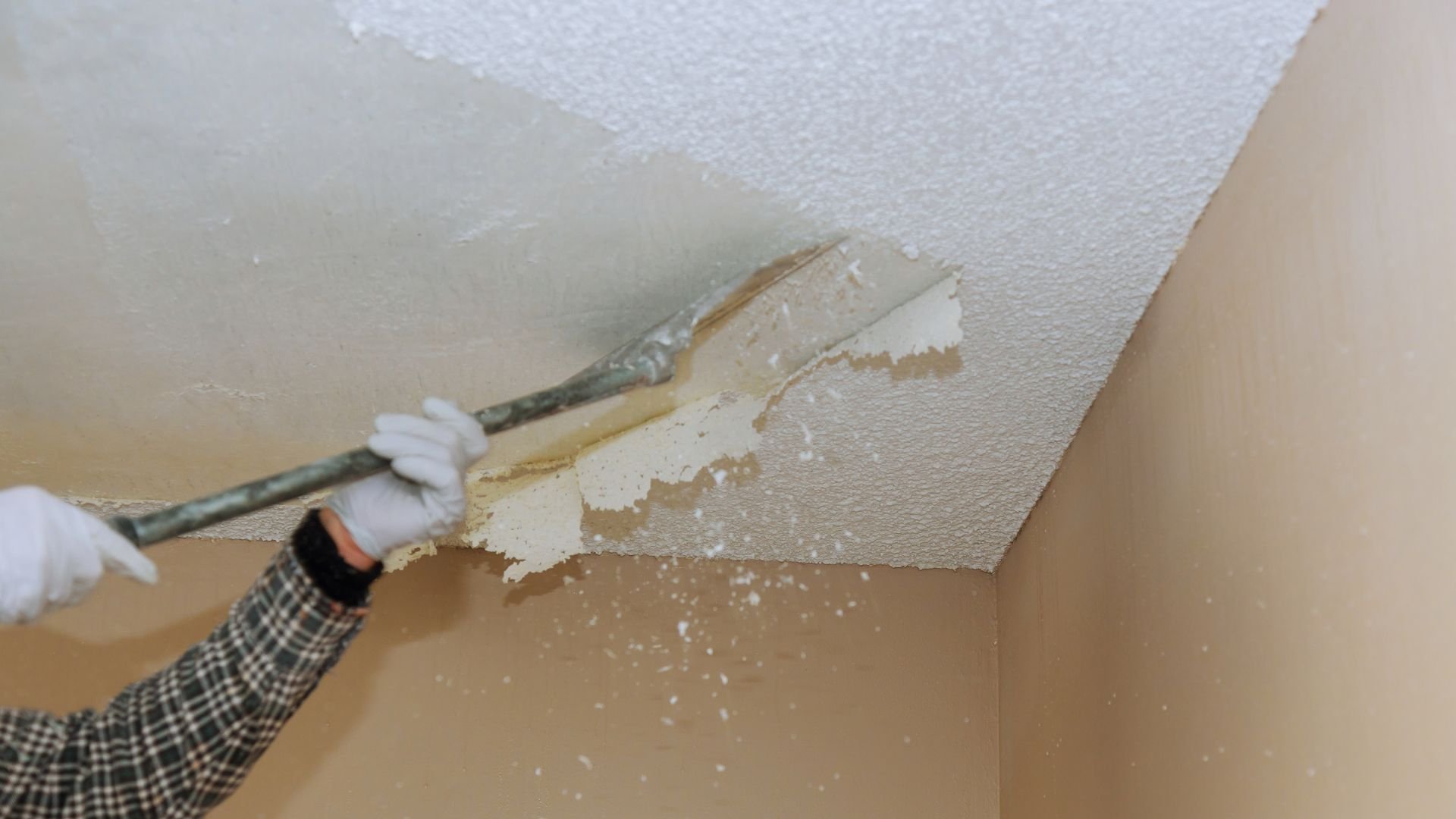 Person scraping popcorn texture from ceiling during home renovation