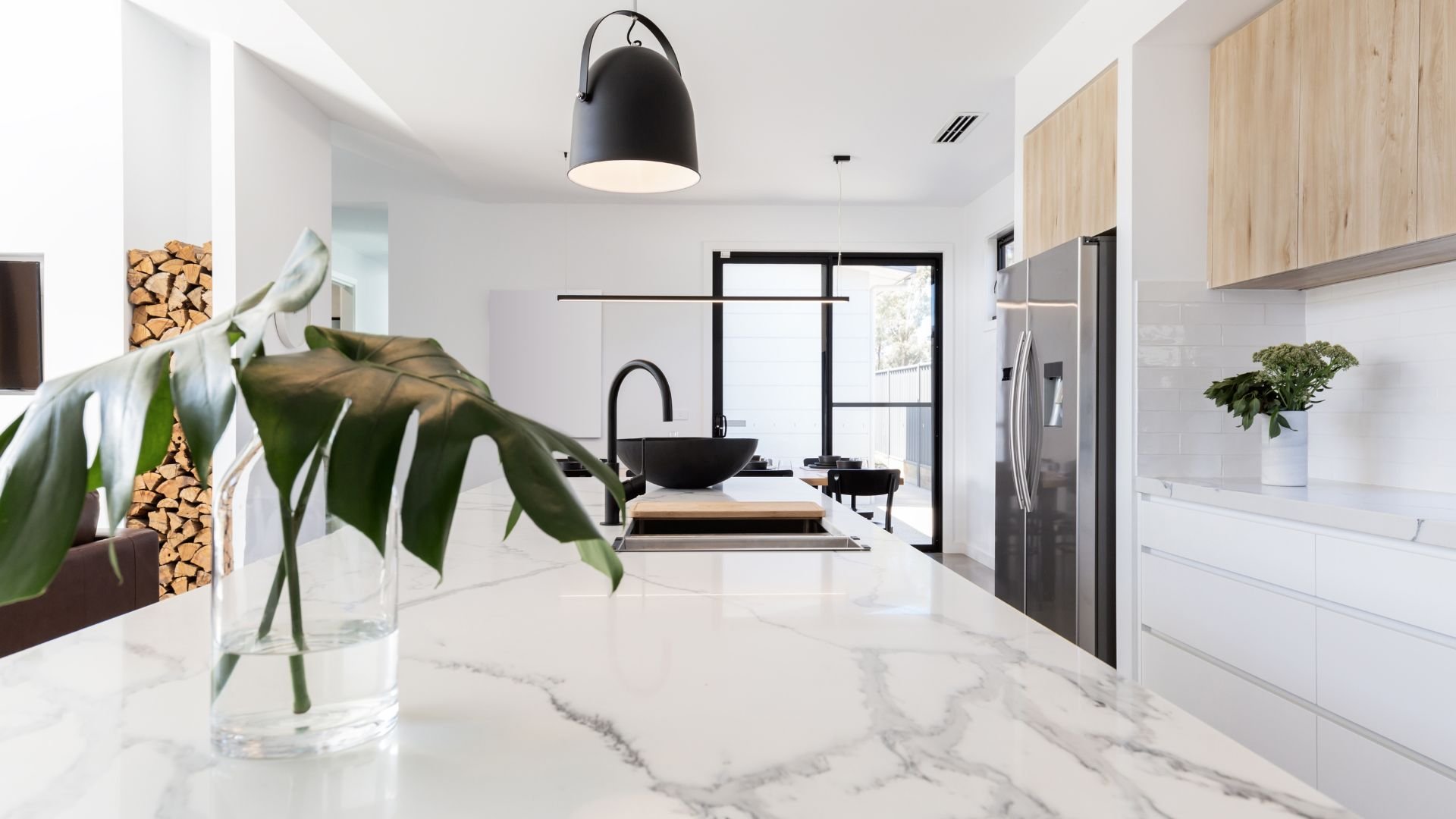 Modern white kitchen with marble countertop, black fixtures, and green plant